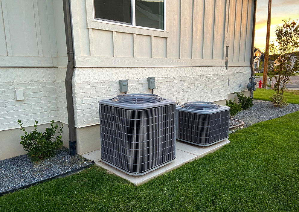 Two outdoor HVAC units sitting outside of a residential home.