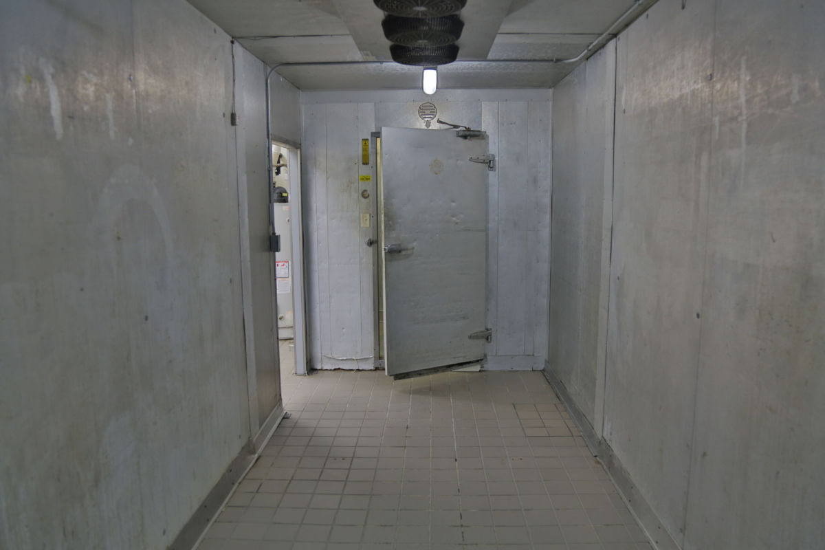 A long hallway leading to a walk-in freezer with the door lightly open.