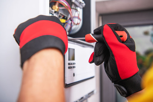 A pair of gloved hands performing a repair on an heating system with a tool.