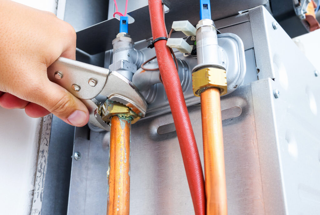 A person's hand using a wrench to perform a service on an HVAC system.