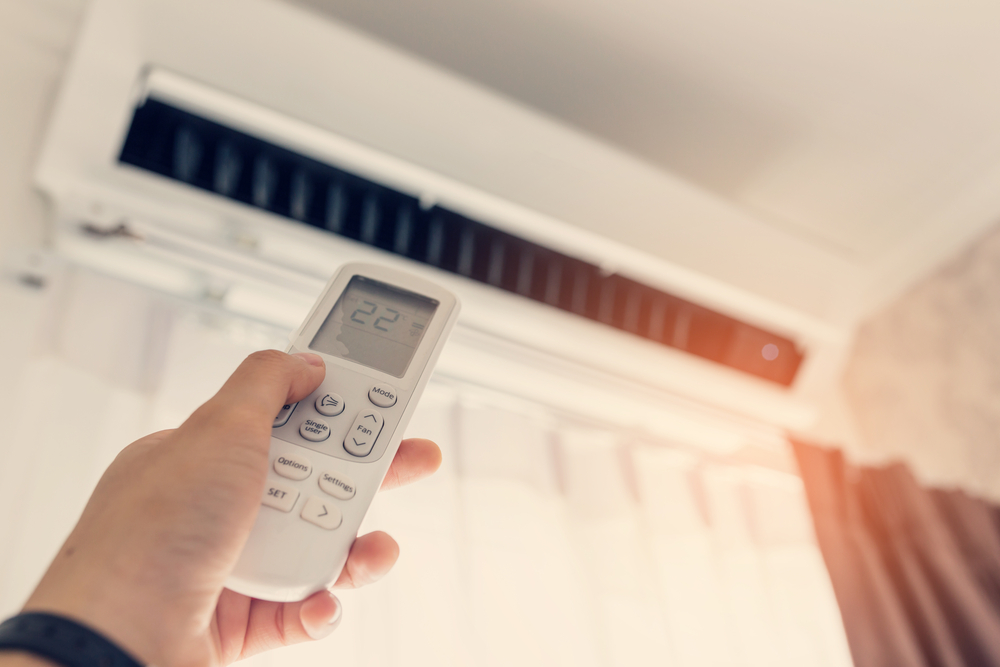 A person using a remote to turn on a ductless mini split system on a wall.